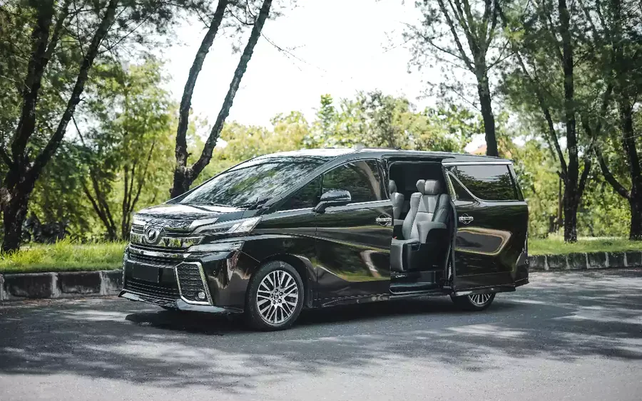 A black Toyota Vellfire MPV parked on a tree-lined road with its sliding door open