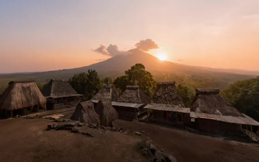 Traditional thatched houses of Moni village at first light with a volcano cone on the horizon