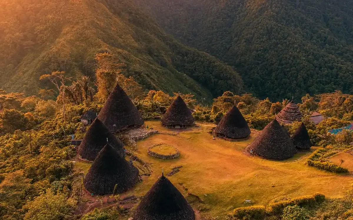 The cone-roofed houses of Wae Rebo in their highland bowl under a sunset sky
