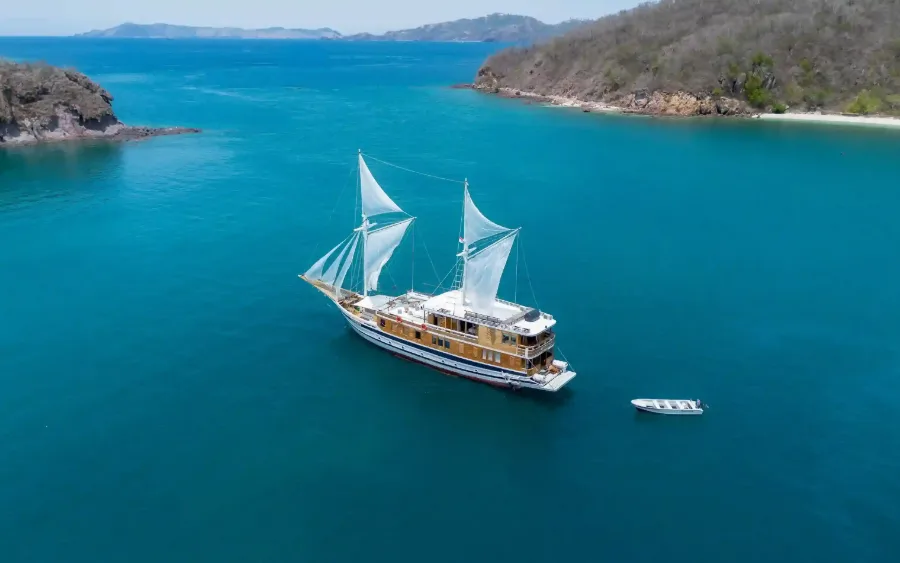 A wooden phinisi liveaboard at anchor with its tender alongside