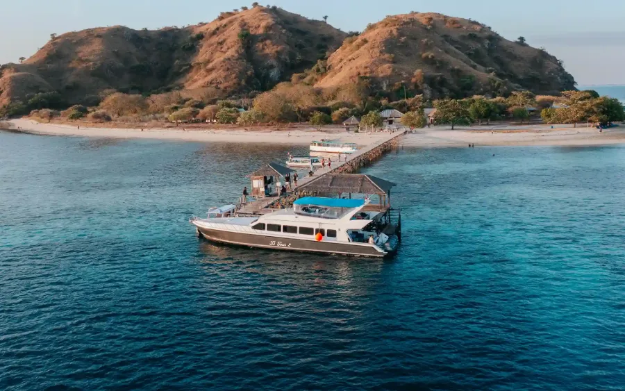 A white day speedboat moored at a jetty in front of dry Komodo hills