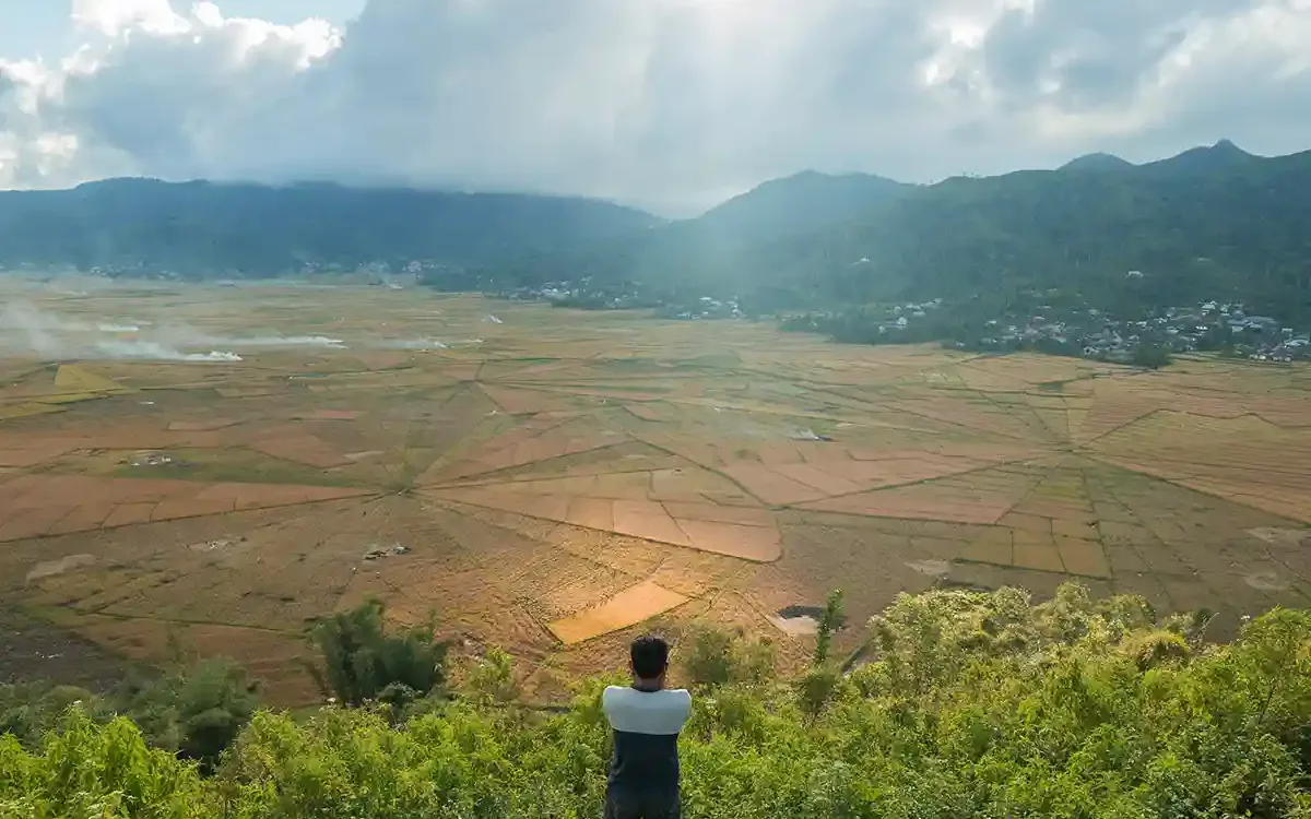 A traveller looking out over the Cancar spider-web rice fields near Ruteng with the Manggarai highlands beyond