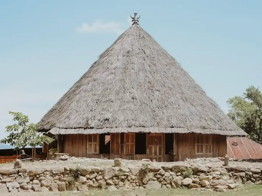 A Manggarai drum house with a buffalo-horn finial above a dry stone wall at the Compang Ruteng ceremonial ground