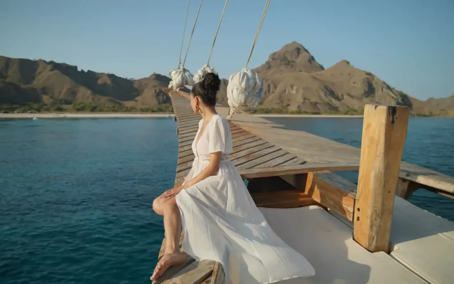 A traditional wooden phinisi anchored in calm water below the dry hills of Komodo National Park