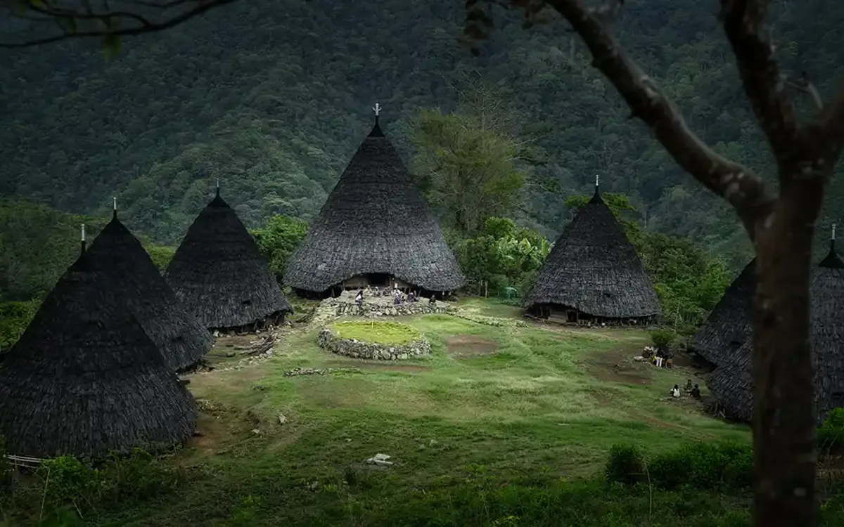 The seven conical mbaru niang houses of Wae Rebo around the ceremonial stone circle, ringed by forested ridges